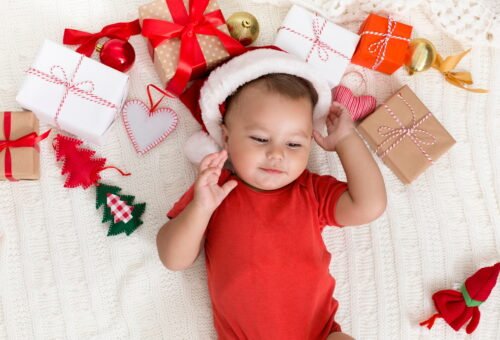Adorable baby in Santa hat napping with Xmas gifts
