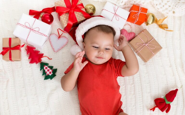 Adorable baby in Santa hat napping with Xmas gifts